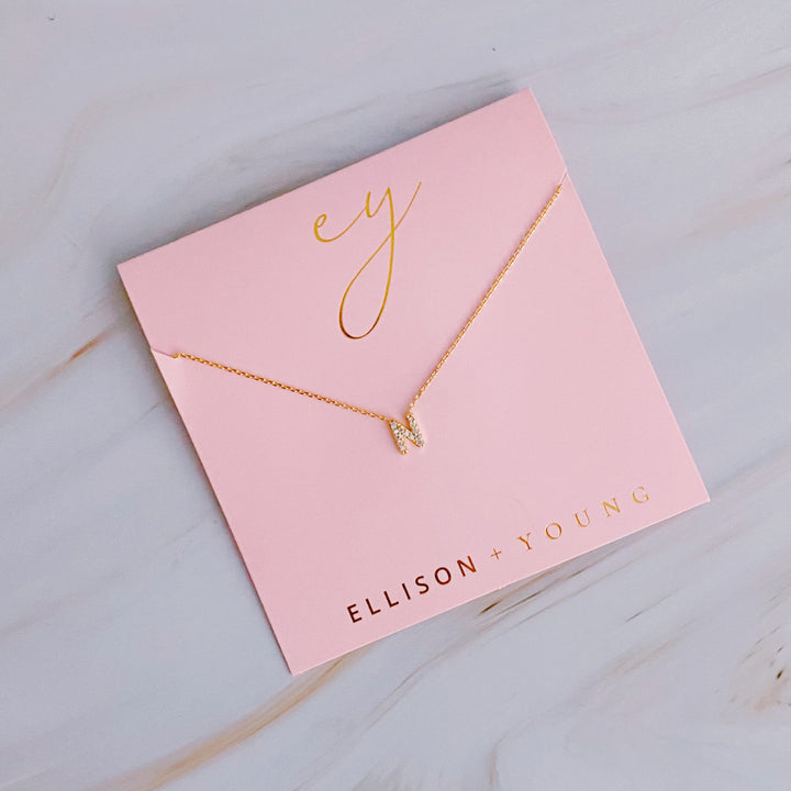 A gold initial "N" pendant necklace on a pink card with "ELLISON + YOUNG" in gold foil.