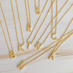 Several gold chains featuring pavé-set crystal initial letter pendants.