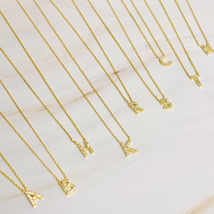 Gold chain necklaces with pavé-set crystal letter pendants displayed on a light surface.