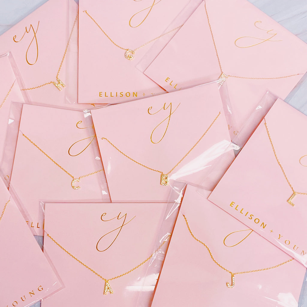 Gold initial pendant necklaces on pink card packaging with the brand name Ellison + Young.