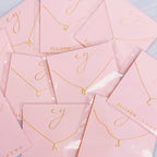 Gold initial pendant necklaces on pink card packaging with the brand name Ellison + Young.