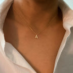 A gold initial pendant necklace featuring a small, pavé-set letter "A" pendant on a delicate chain.