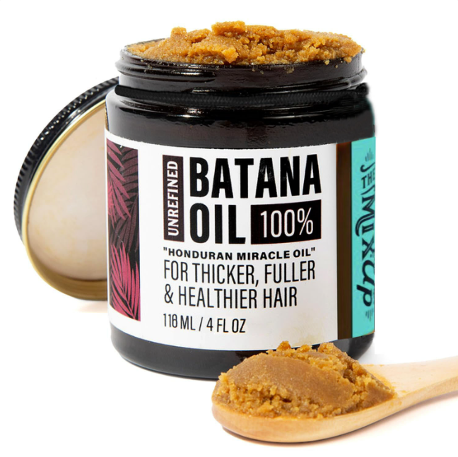 An open black jar of brown Glow Restore Hair Mask with a wooden spoon holding a scoop in front.