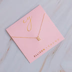 A gold initial "E" pendant necklace on a pink display card.