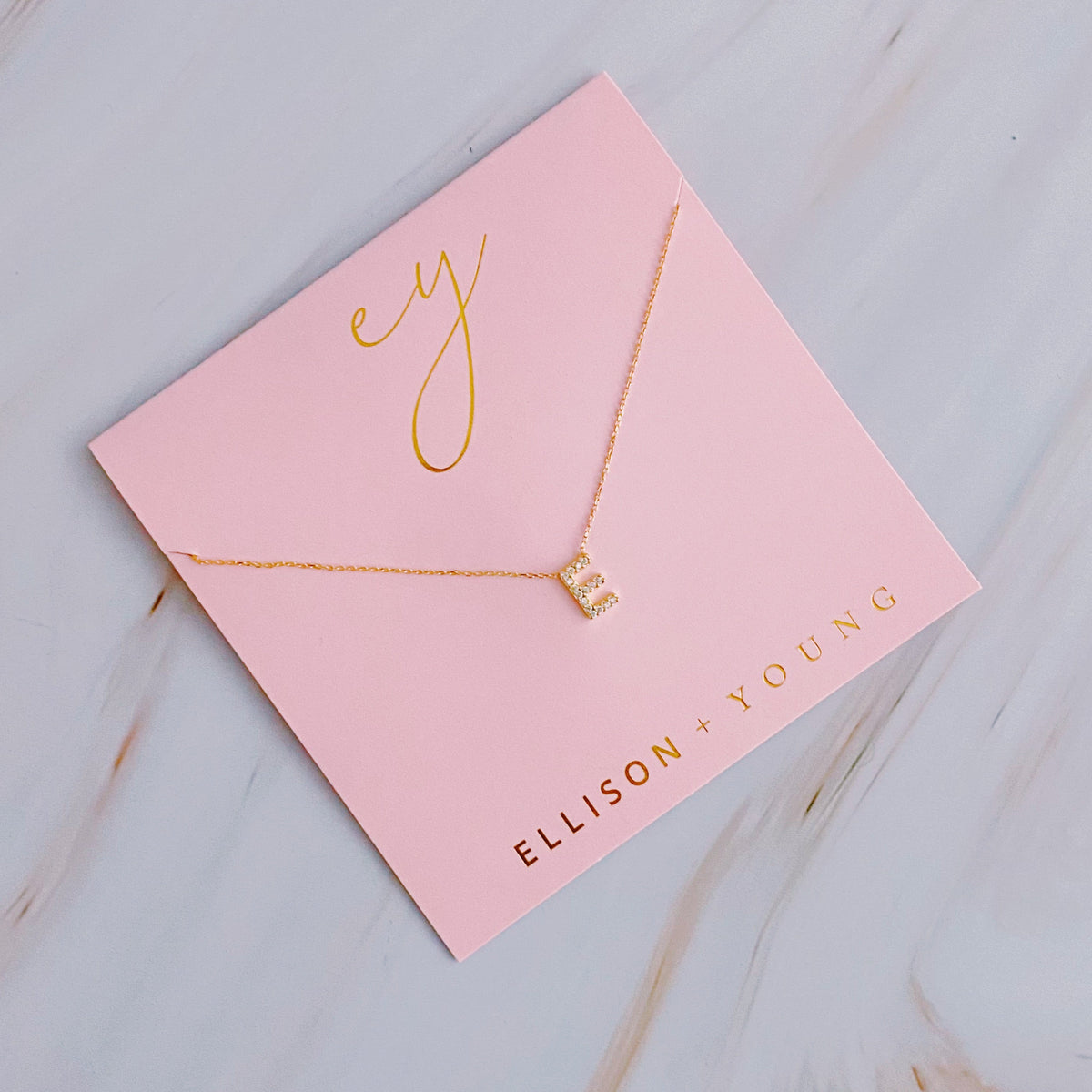 A gold initial "E" pendant necklace on a pink display card.