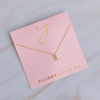 Gold initial R necklace with pavé crystals on a pink Ellison + Young card.