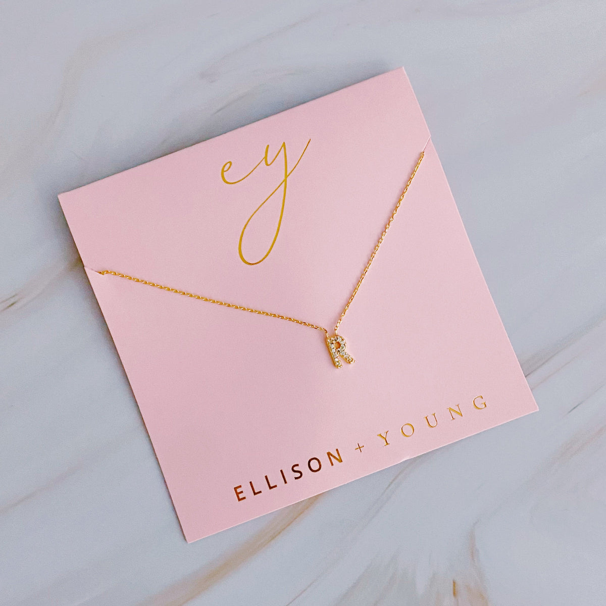 Gold initial "R" pendant necklace displayed on a pink packaging card.