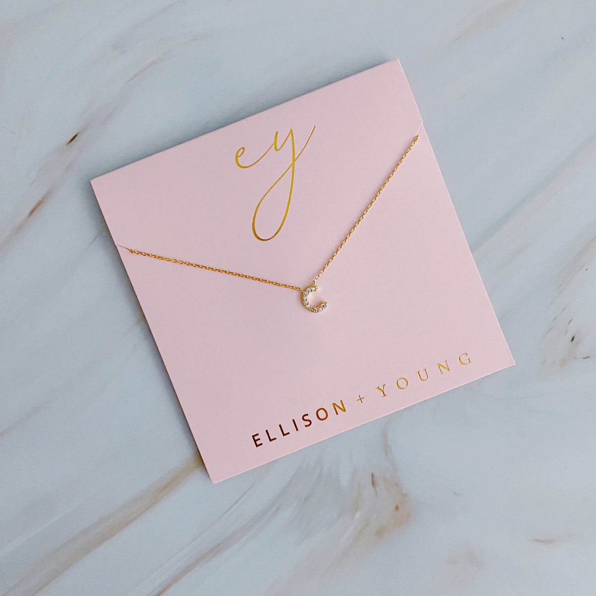 Gold initial C pendant necklace on a pink card with gold branding.