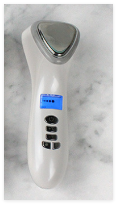 White facial massager with a triangular silver head, blue digital display, and control buttons.