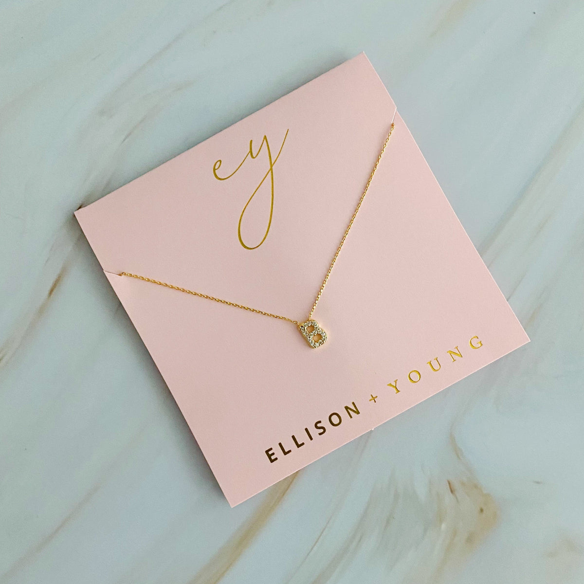 Gold initial B pendant necklace on a pink card with "ELLISON + YOUNG".