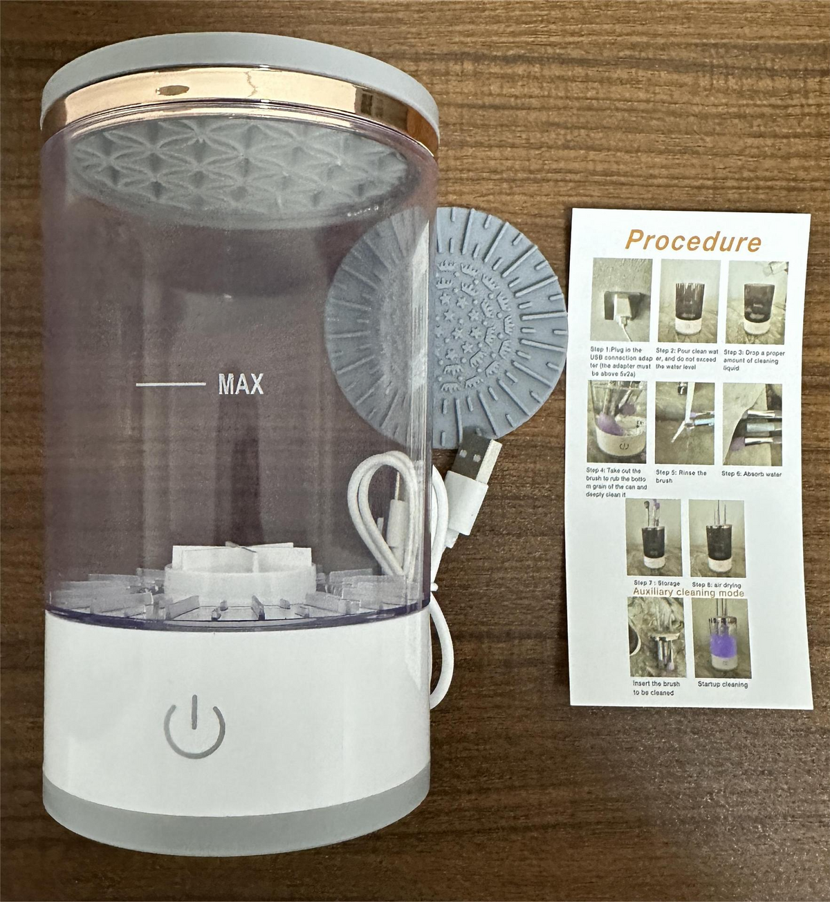 Clear cylinder makeup brush cleaner with a white base, power button, USB cord, and instruction manual.