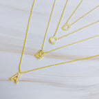 Four gold chain necklaces with crystal-paved initial pendants spelling A, B, C, and D.