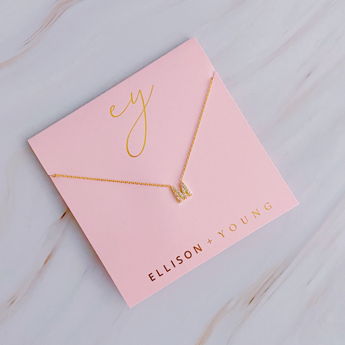Gold initial pendant necklace on pink card with "ELLISON + YOUNG" and "ey" in gold lettering.
