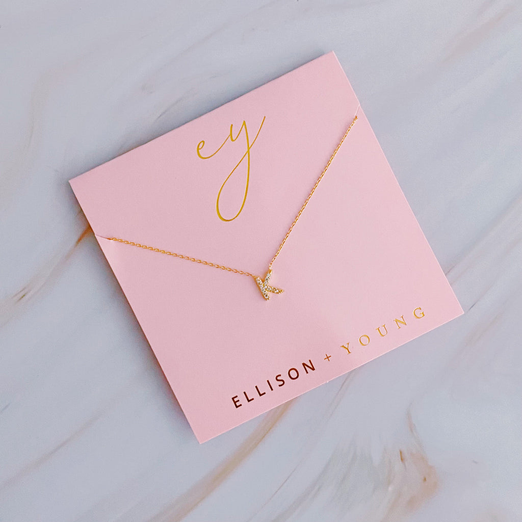 Gold initial K pendant necklace on a pink card with gold lettering and brand logo.