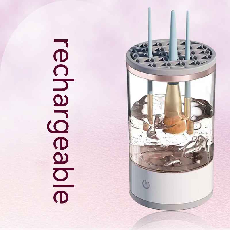 A rechargeable makeup brush cleaner with a clear cylinder, white base, and patterned grey lid holding three brushes in water.