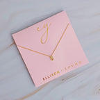 A gold chain necklace with a crystal-embellished letter S pendant on pink packaging.