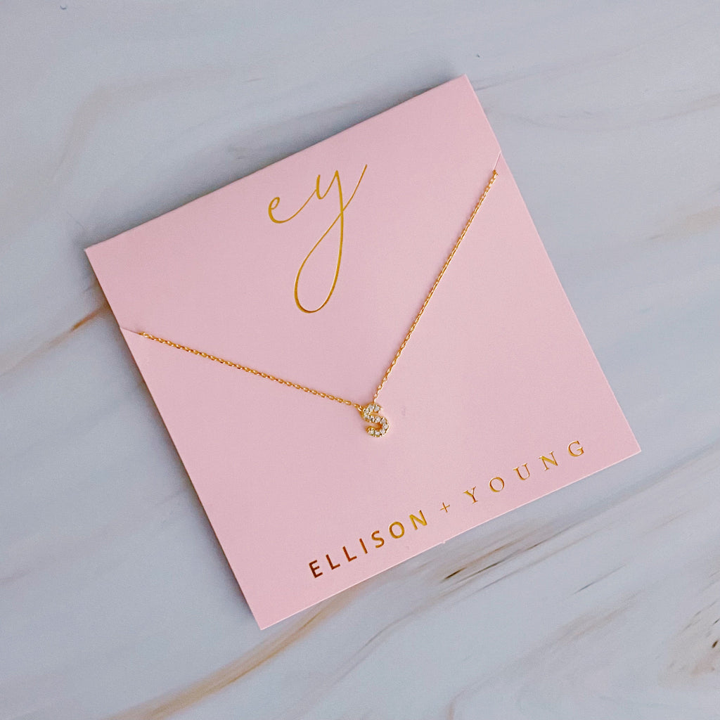 Gold chain necklace with initial 'S' pendant mounted on pink Ellison + Young backing card.