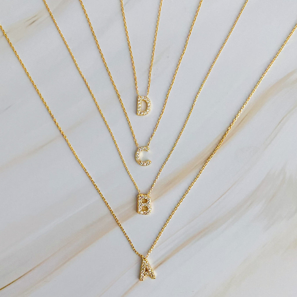 Four gold initial pendant necklaces with crystal-encrusted letters A, B, C, and D.