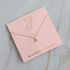Gold initial pendant necklace featuring letter A on pink packaging branded Ellison + Young.